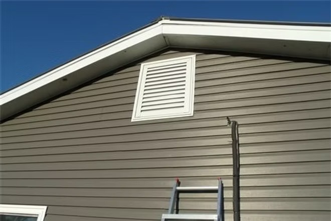 Hinged gable vent closed on a gray-sided gable